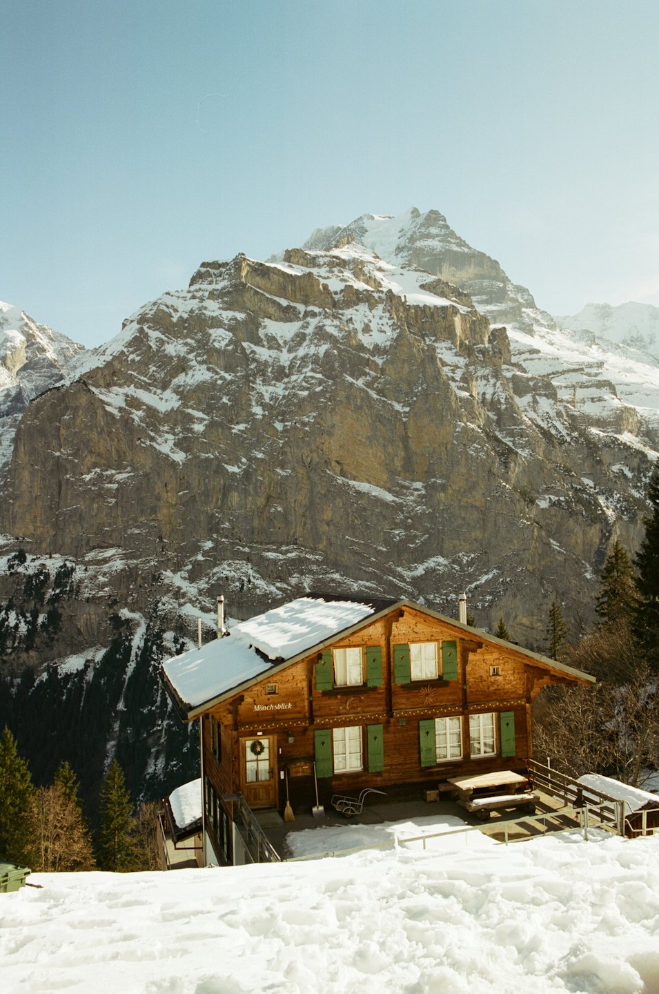 Acogedor chalet de madera con contraventanas verdes en un paisaje de montaña nevado.