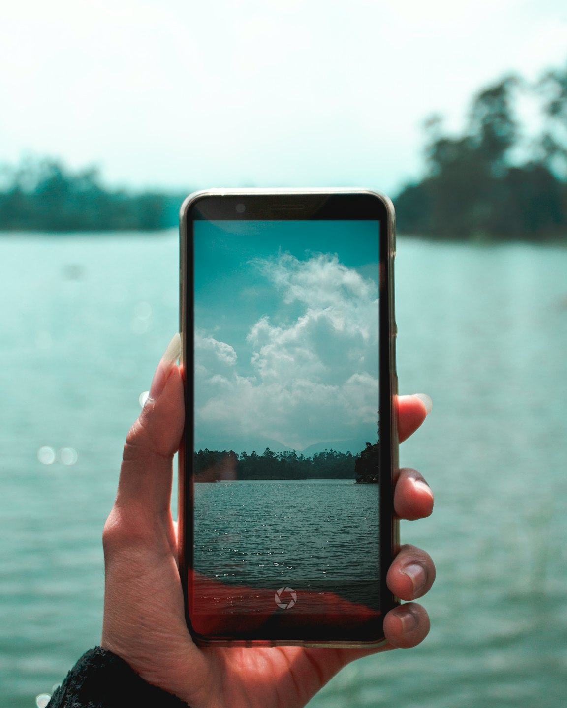 Una mano sostiene un smartphone capturando una vista panorámica del lago.