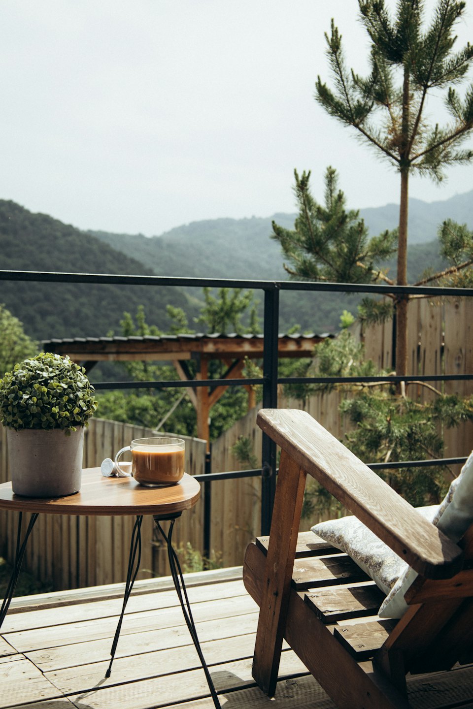 Mesa redonda con café y planta en un balcón con vistas a la montaña.