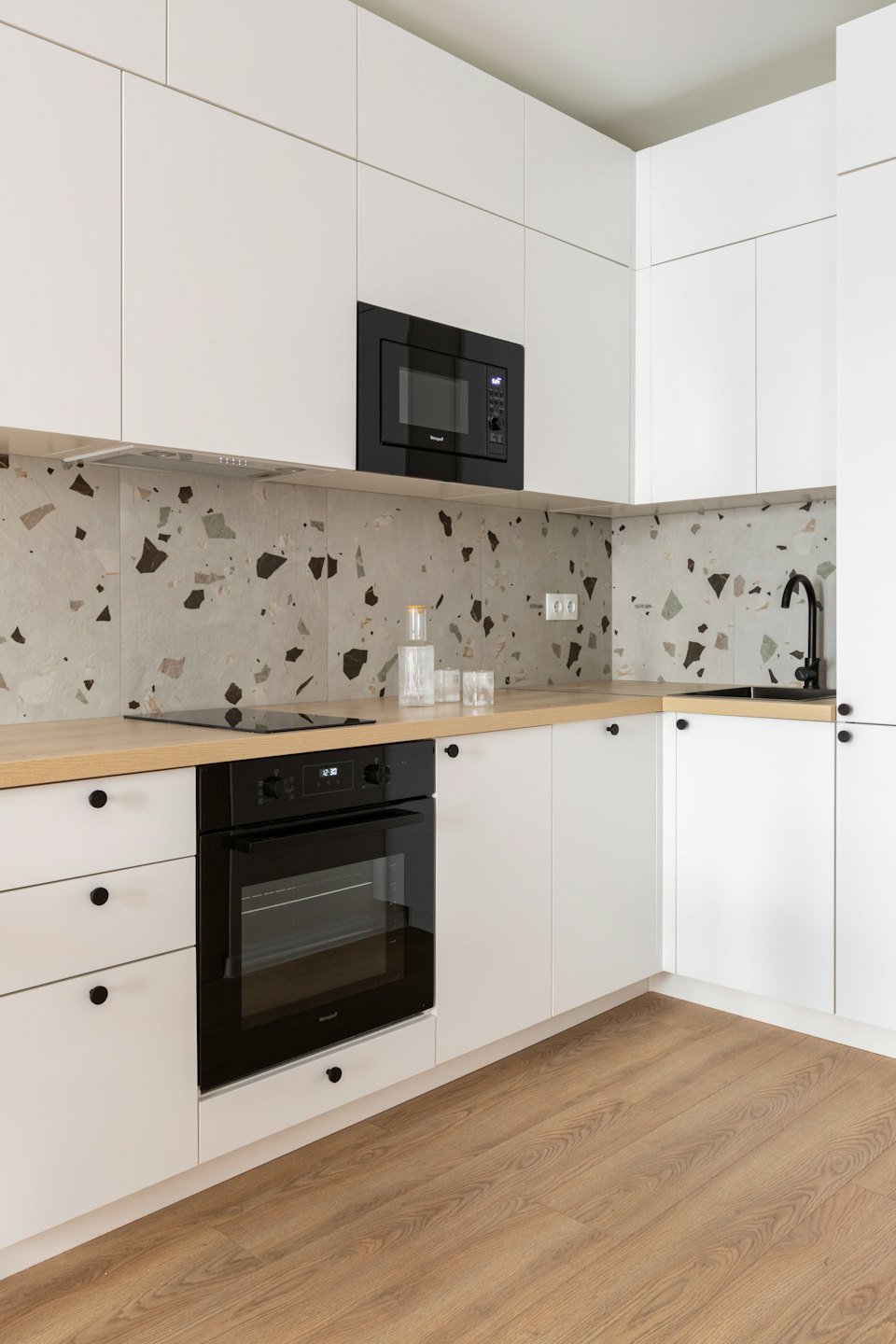 Cocina moderna con gabinetes blancos, encimeras de madera y salpicadero de terrazo.