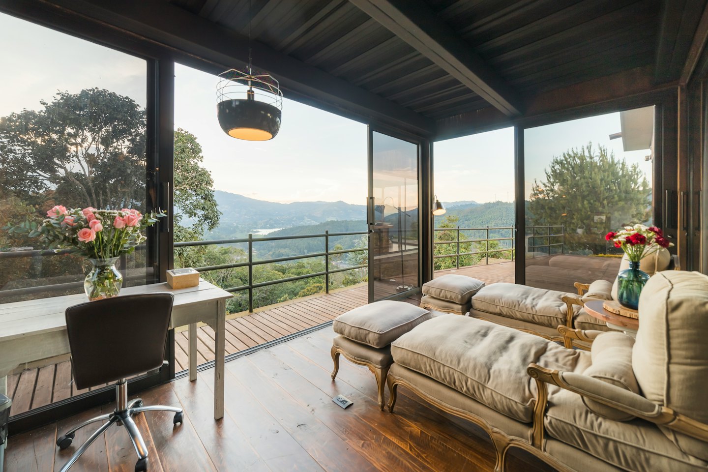 Moderna sala acristalada con escritorio y sillones con vistas a un valle montañoso.