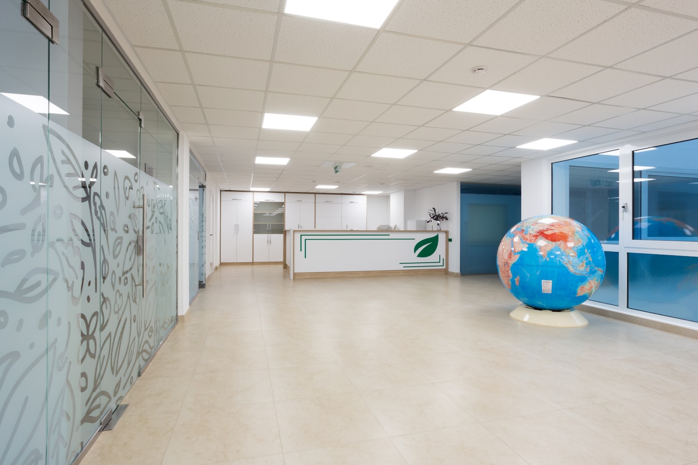 Escritorio de recepción de oficina moderno con globo terráqueo y mamparas de vidrio esmerilado.