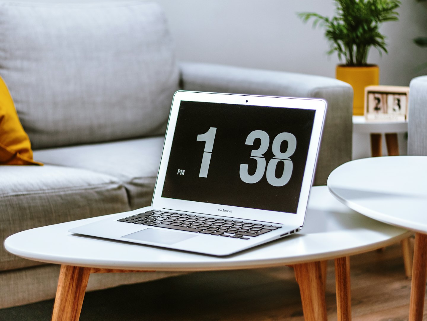 Portátil plateado con un reloj sobre una mesa de centro blanca.