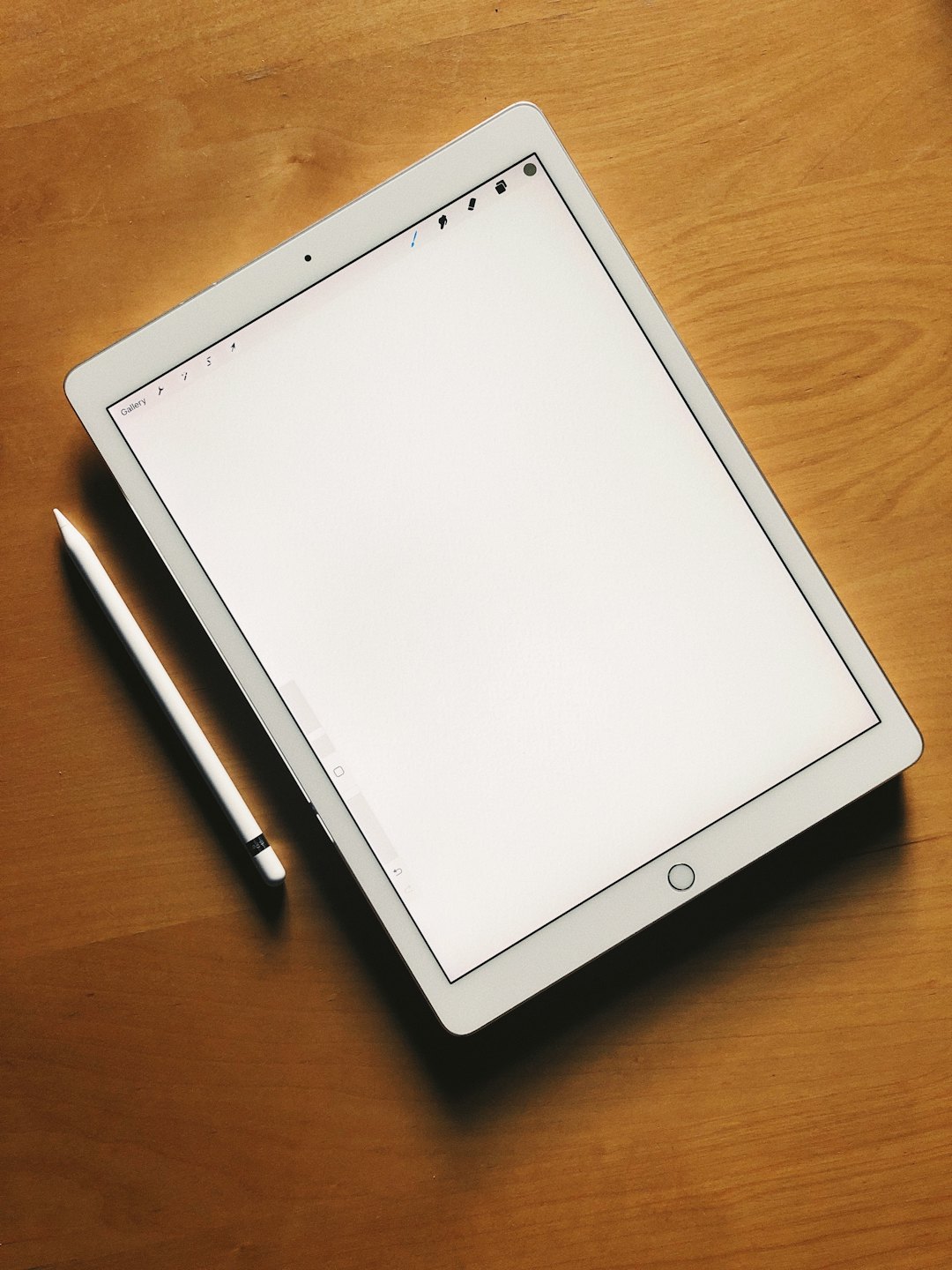 Una tableta digital blanca y un lápiz óptico descansan sobre un escritorio de madera.