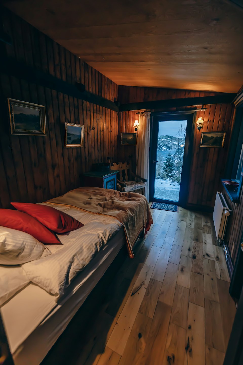 Un dormitorio rústico con ropa de cama blanca tiene vistas a un paisaje nevado.